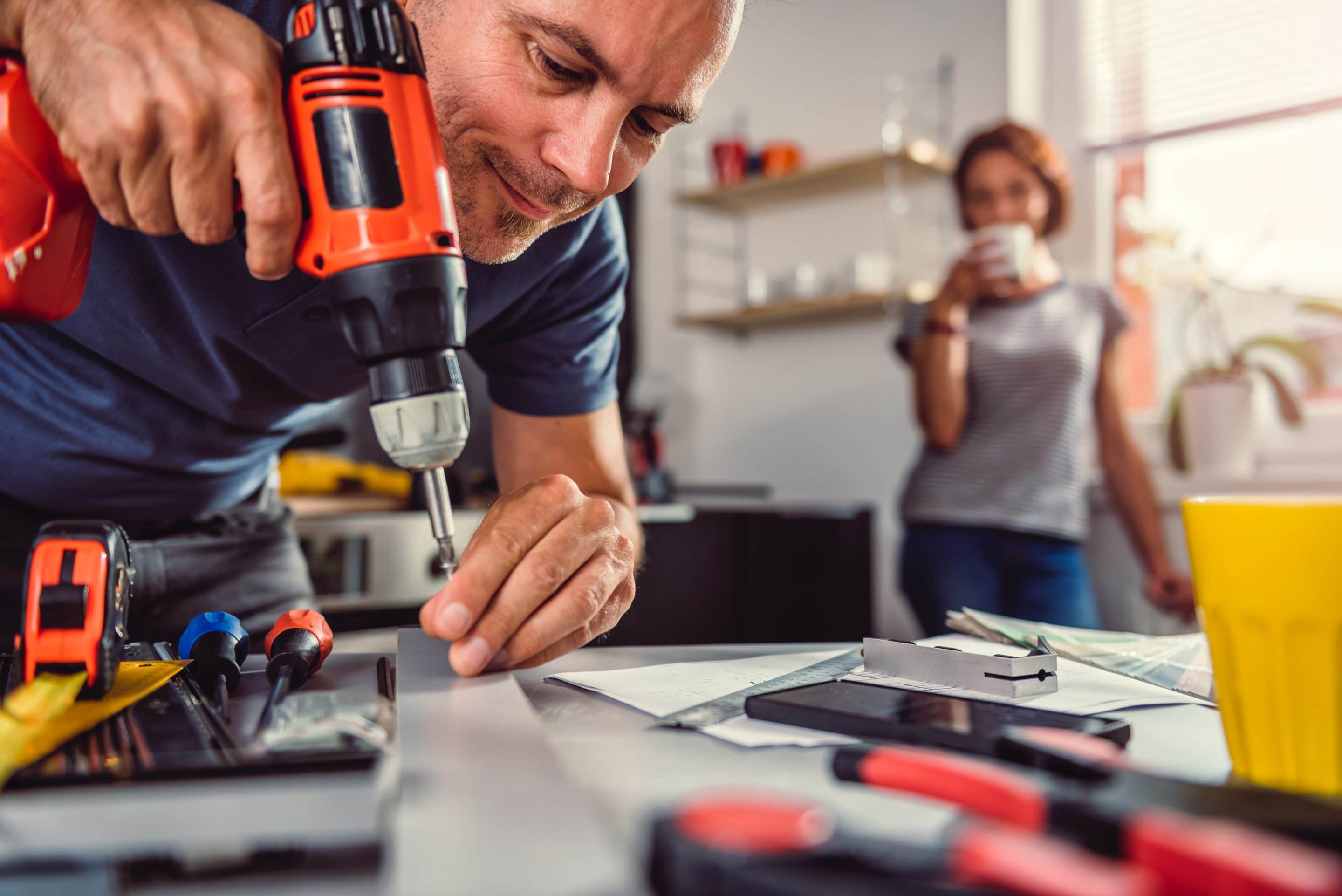 homme qui visse un objet pendant qu'une cliente le regarde dans sa cuisine